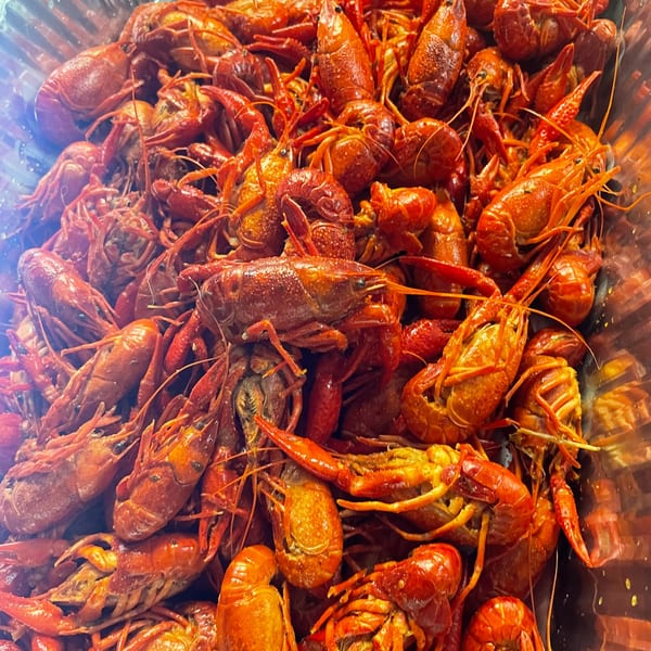Close-up of a large metal tray filled with bright red, cooked crawfish.