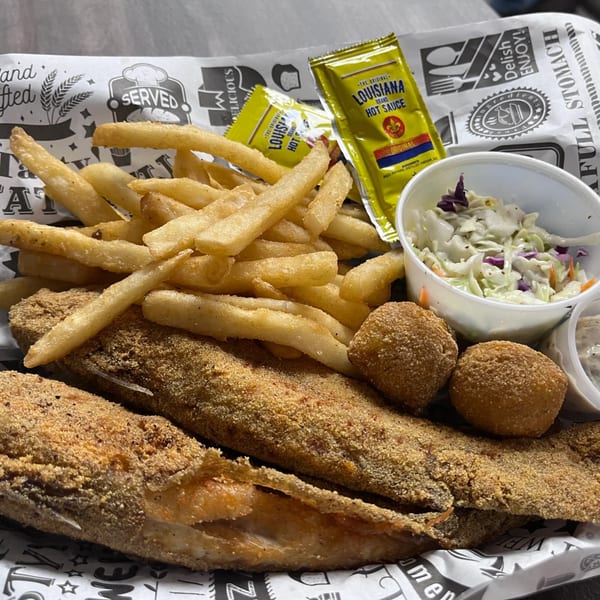 Fried Delta Fish Market catfish, hushpuppies, fries, coleslaw, and Louisiana hot sauce packets.
