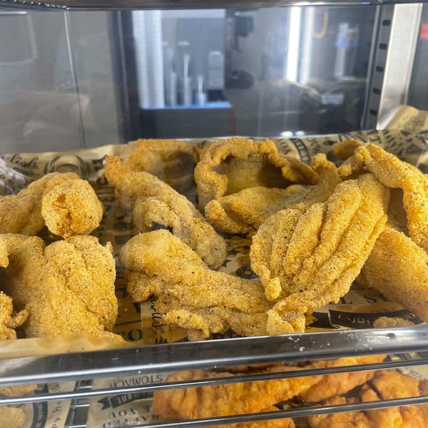 Close-up of golden-brown fried fish fillets in a display case, resting on patterned paper.