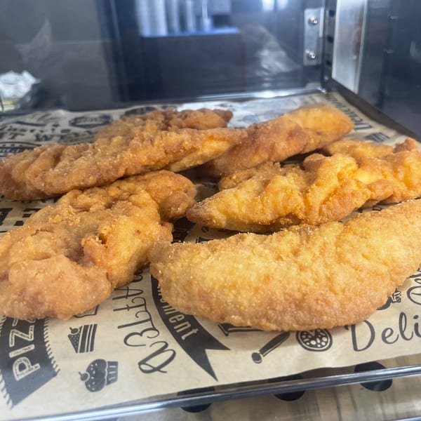 Golden-brown fried chicken tenders arranged on a sheet of patterned parchment paper.