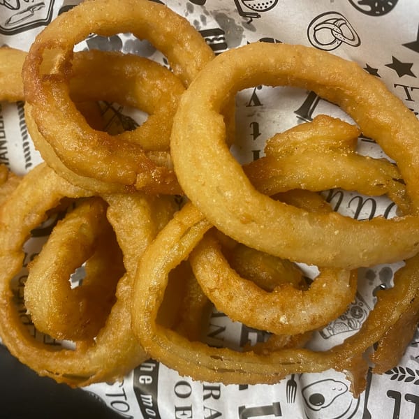 Golden-brown, crispy onion rings piled on white paper with black food-themed illustrations.