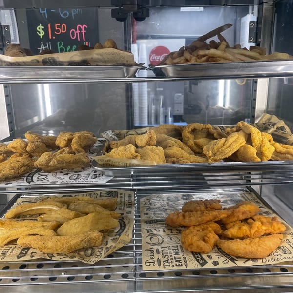 A display case filled with trays of fried fish, chicken tenders, and french fries.