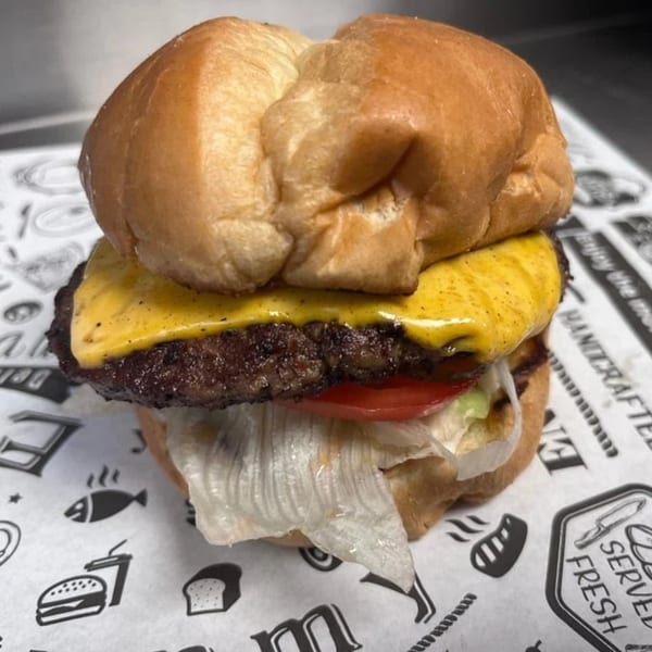 Cheeseburger with melted cheese, tomato, and lettuce on a bun, on branded Delta Fish Market paper.