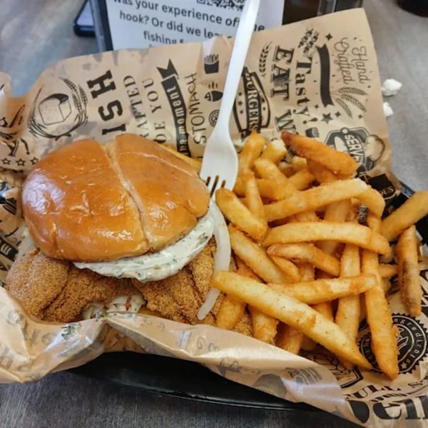 A Delta Fish Market fried fish sandwich with tartar sauce and onions, served with golden french fries.