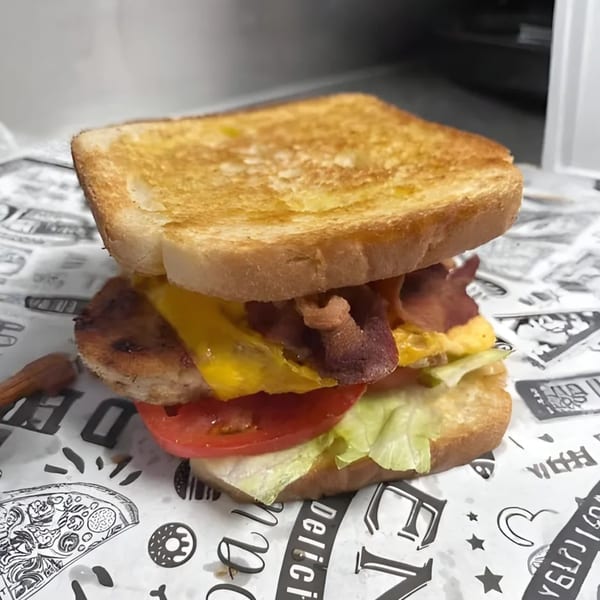 Grilled fish sandwich with melted cheese, bacon, tomato, and lettuce on toasted bread.